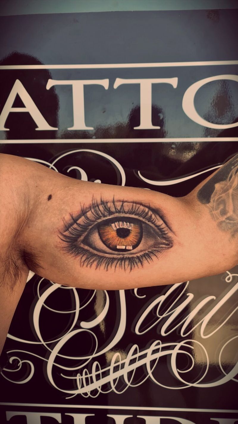 Photorealistic eye with an amber iris tattooed on an inner forearm