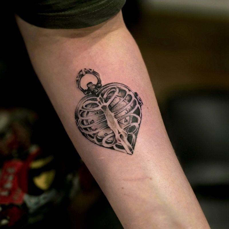 Black and grey heart-shaped locket opening to a ribcage, tattooed on a forearm
